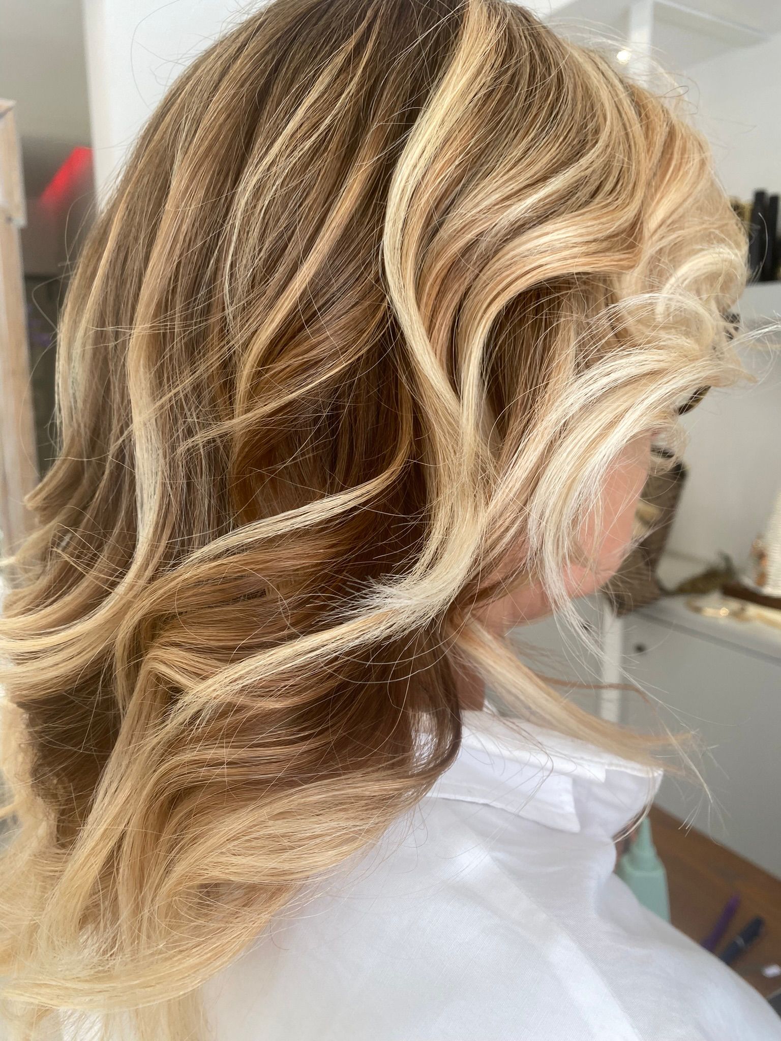 Capelli ondulati castani con schiariture bionde dorate, visti di profilo su camicia bianca in un salone luminoso